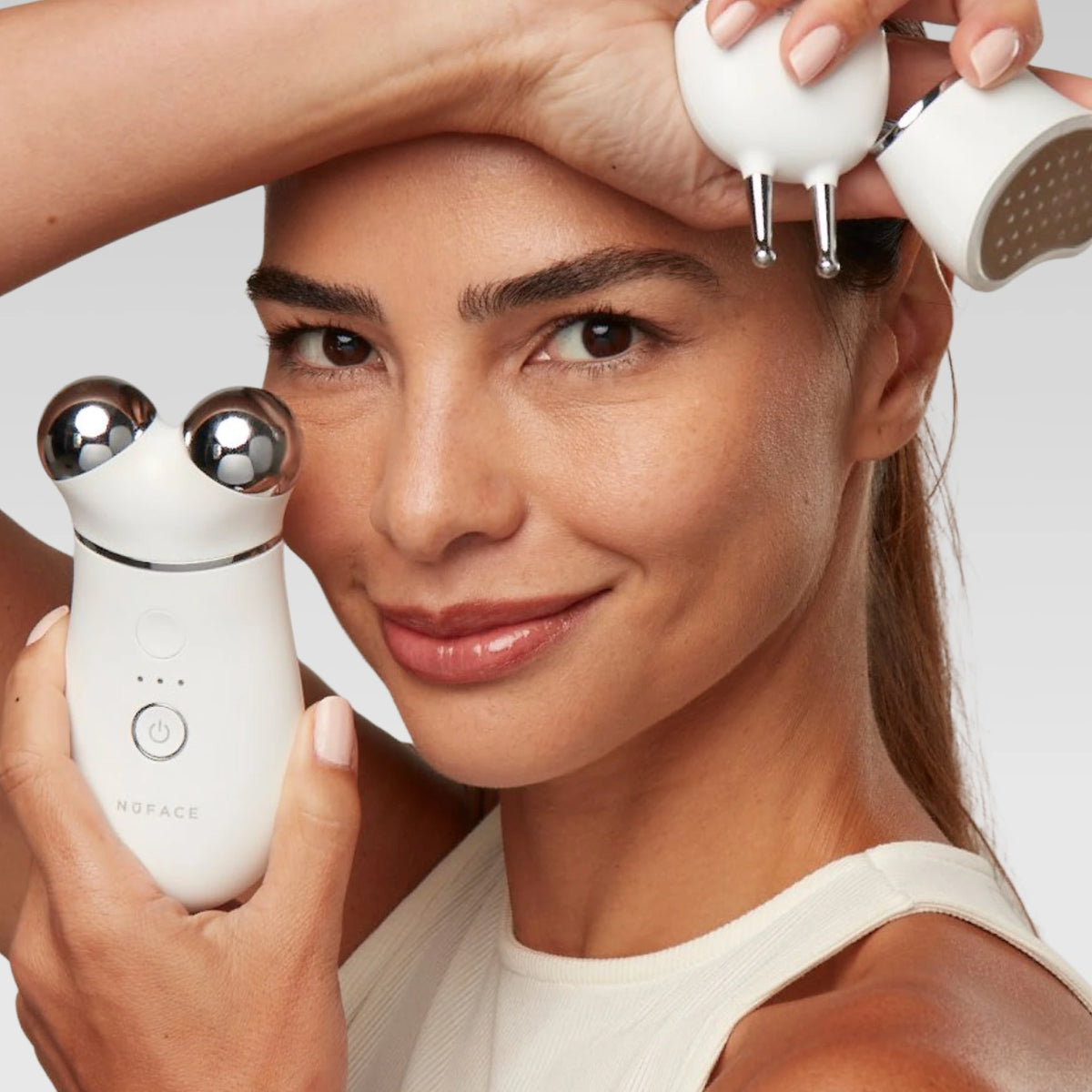 Woman holding NuFACE attachments for TRINITY+ device against her face on a light background